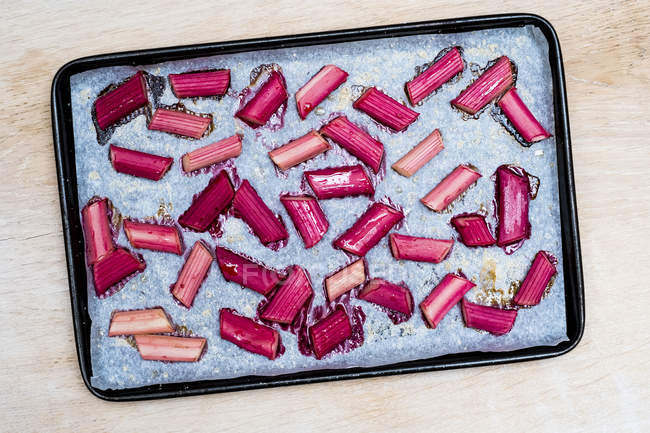 High angle close-up of slices of rhubarb on paper on baking tray. — Stock Photo