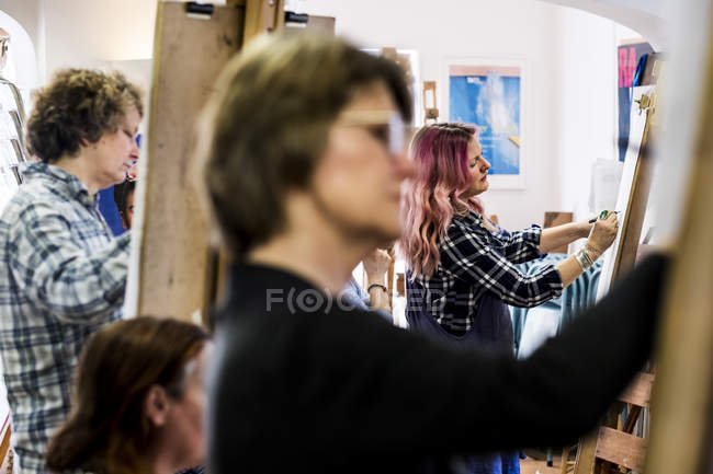 Focus selettivo sulle donne in piedi ai cavalletti e disegno in classe d'arte . — Foto stock
