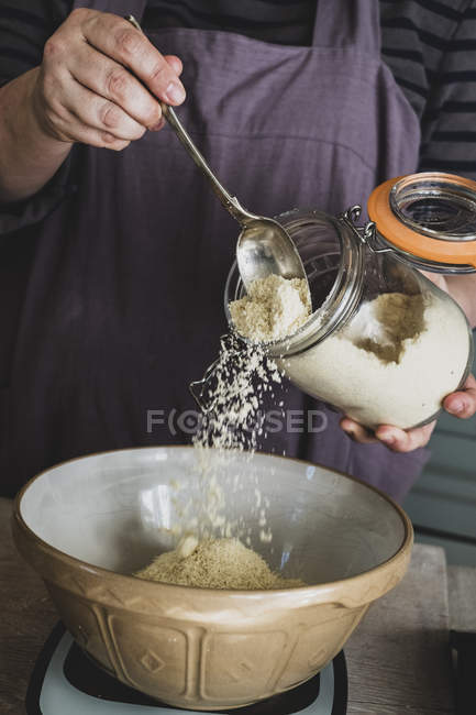 Midsection of person pouring sugar into mixing bowl with baking ingredients. — Stock Photo