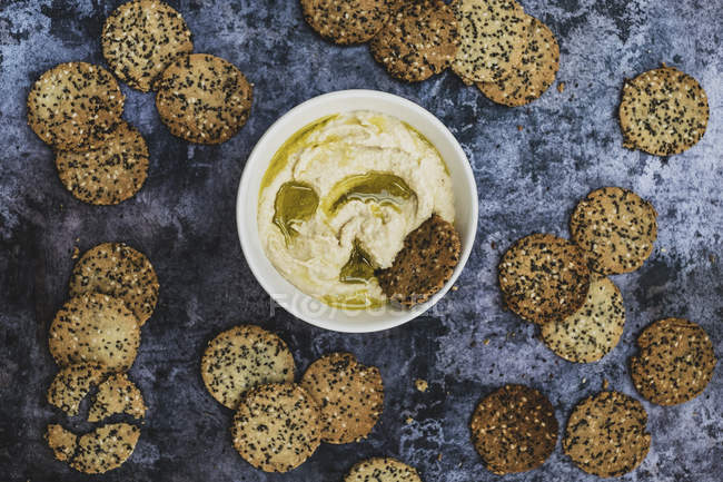 Top view of bowl of hummus and freshly baked seeded crackers. — Stock Photo