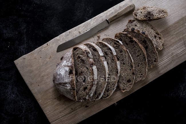 Високий кут зору скибочок хліба свіжого коричневого хліба на дошці з гострим ножем — стокове фото