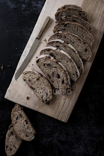 Vista ad alto angolo di fette di pagnotta di pane fresco marrone a bordo con coltello affilato — Foto stock