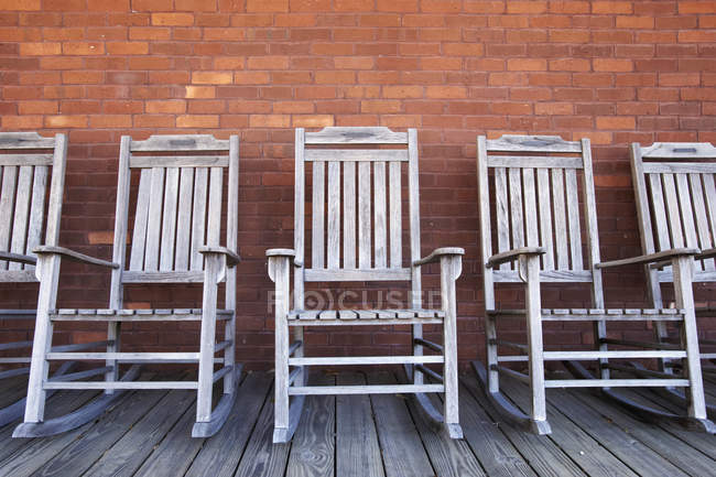 Fila de cadeiras de balanço de madeira contra a parede de tijolo — Fotografia de Stock
