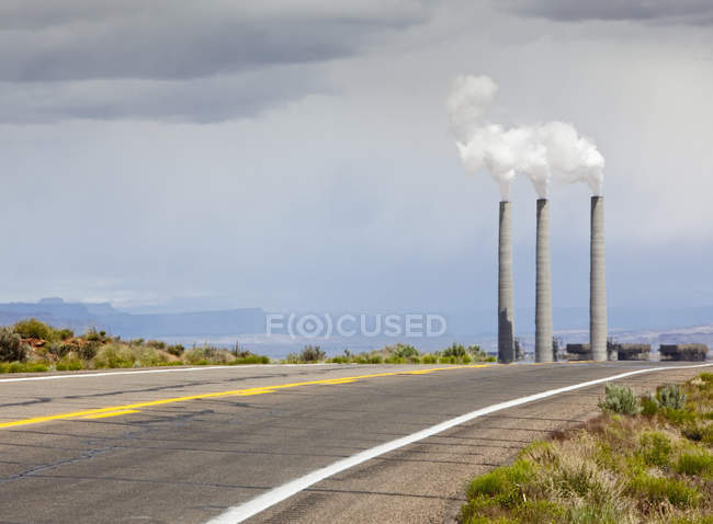 Estrada do deserto que leva a chaminés de fumaça de planta industrial no Arizona, EUA — Fotografia de Stock