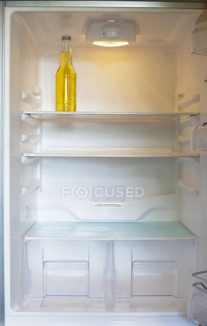 Bottle in clean refrigerator with empty shelves — Stock Photo