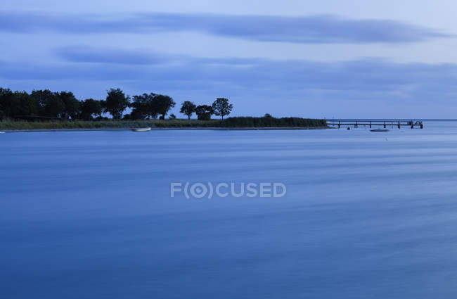 Dusk over calm water surface and coastline with trees and boats moored offshore in Denmark — Stock Photo