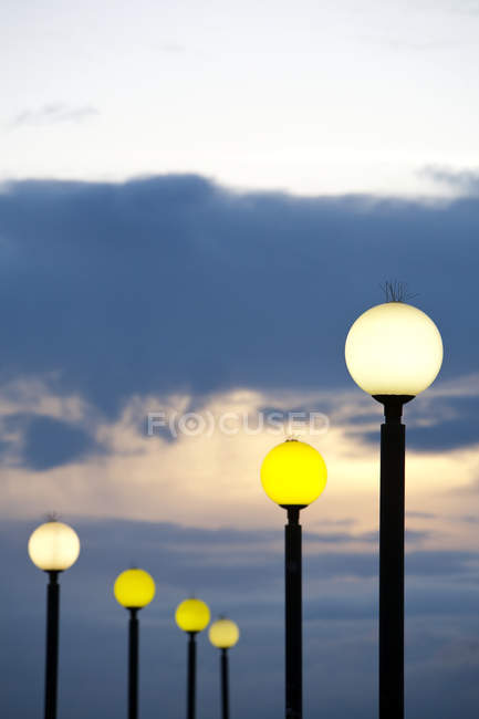 Réverbères ronds s'illuminant au crépuscule contre un ciel nuageux — Photo de stock