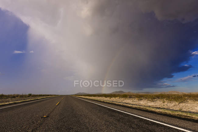 Storm and rainbow along highway road in desert — Stock Photo