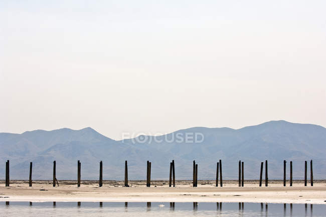 Postos de madeira com reflexão em água e montanhas à distância — Fotografia de Stock