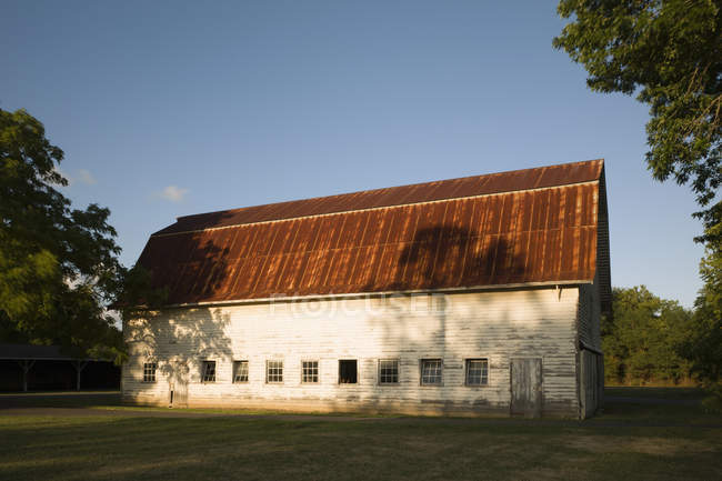 Farm building with red rusty roof and shingle walls and row of windows low in wall. — Stock Photo