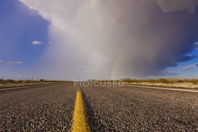 Tormenta y arco iris a lo largo de carretera en el desierto - foto de stock