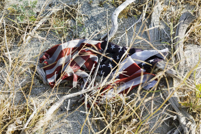 American flag, crumpled up on sandy ground and damaged — Stock Photo