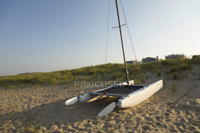 Catamaran sailing boat on sandy beach with houses in distance. — Stock Photo