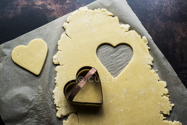 Primo piano ad angolo alto dei biscotti a forma di cuore tagliati dalla pasta dei biscotti sulla carta da forno . — Foto stock