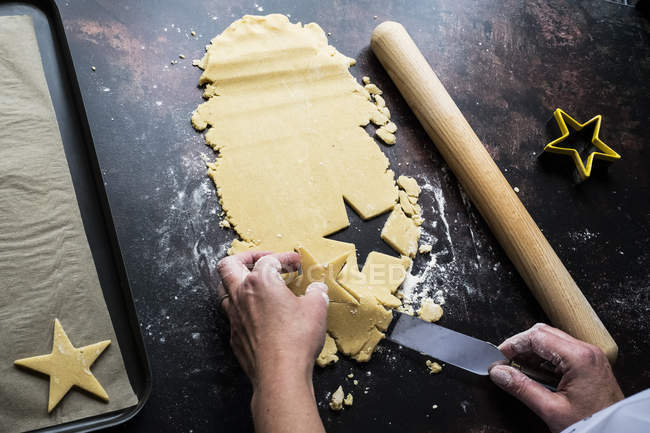 High angle close-up of cook lifting cut out star-shaped cookies onto baking tray with palette knife. — Stock Photo