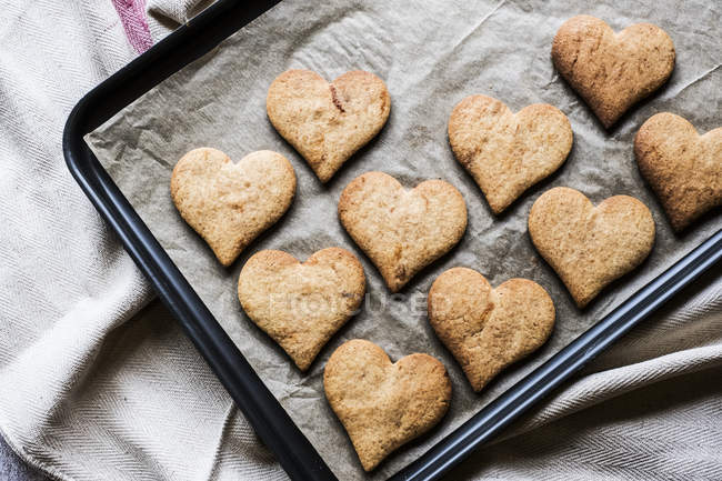 Primer plano de ángulo alto de galletas recién horneadas en forma de corazón en bandeja para hornear . - foto de stock