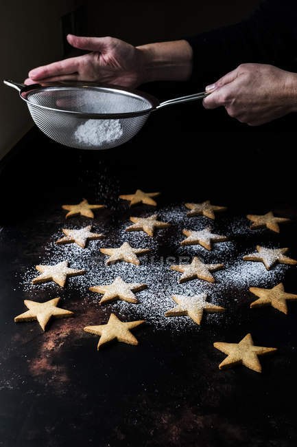 Мужчина-повар вытирает пыль из свежеиспеченного печенья в форме звезды с ледяным сахаром через решето . — стоковое фото