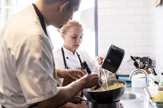 Чоловічий і жіночий кухарі в коричневих фартухів стояти на кухні лічильник, виготовлення голландським соусом. — стокове фото