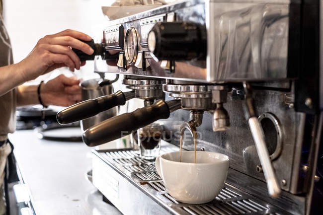 Close-up of hands of female barista making cappuccino using commercial coffee machine. — Stock Photo