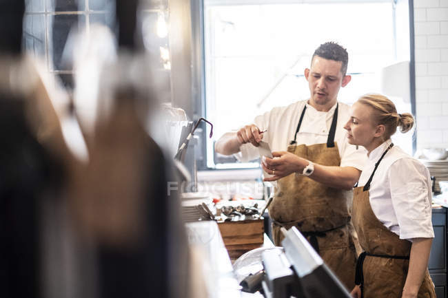 Male and female chefs in brown aprons standing at counter and checking order. — Stock Photo