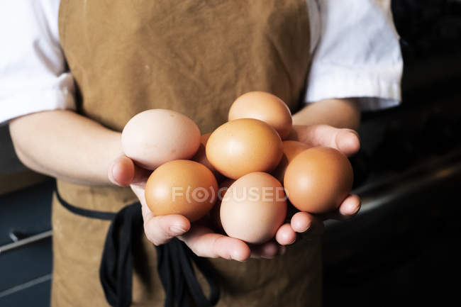 Close-up of hands of woman wearing apron holding fresh brown chicken eggs. — Stock Photo
