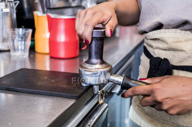 Female barista preparing coffee, tamping into machine holder in cafe. — Stock Photo