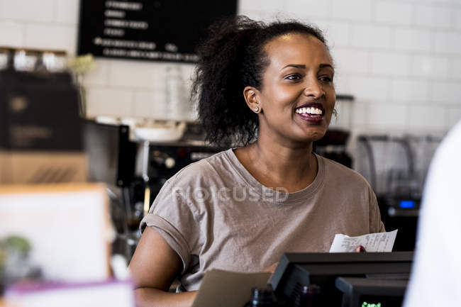 Female barista smiling in welcome beside counter in coffee shop. — Stock Photo