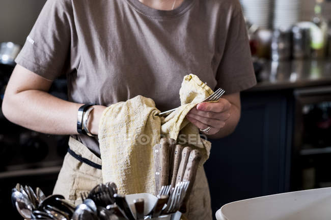 Midsection of staff member drying cutlery in cafe. — Stock Photo