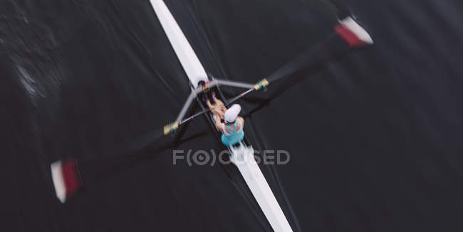 Overhead view of oarsman in single scull boat on calm water mid stroke, motion blur. — Stock Photo