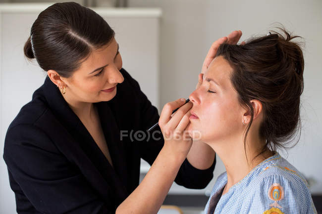 Professional make-up artist at work, creating look with brush for young woman. — Stock Photo