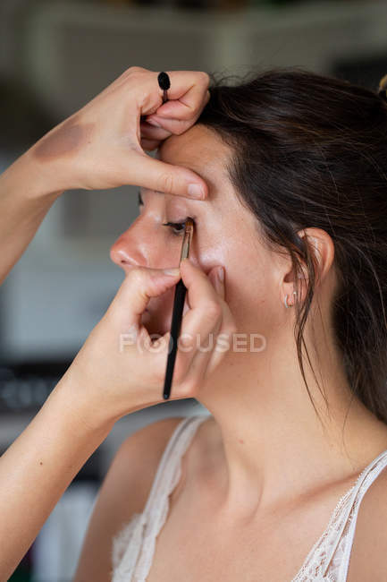 Artista de maquiagem profissional no trabalho, criando olhar com escova para mulher jovem . — Fotografia de Stock