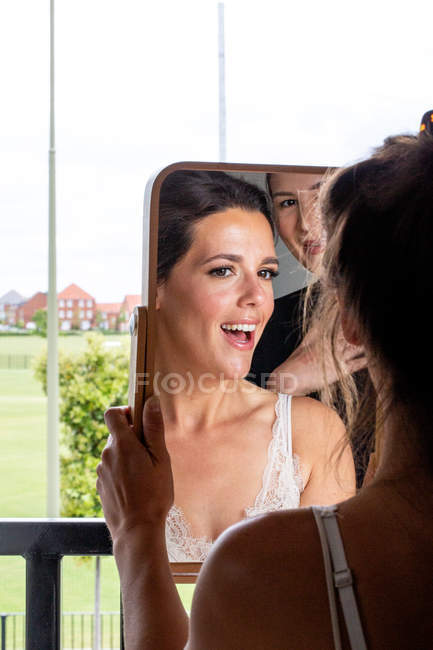 Professional make-up artist and smiling woman holding and looking in mirror. — Stock Photo