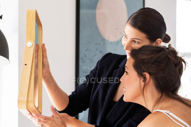Professional make-up artist and smiling woman holding and looking in mirror. — Stock Photo