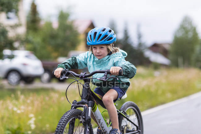 Elementary idade menino de corrida de bicicleta na estrada chuvosa . — Fotografia de Stock