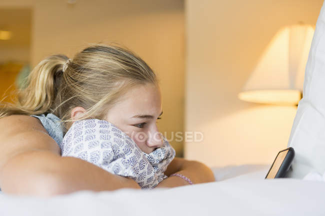 Menina adolescente deitada na cama do quarto do hotel olhando para o smartphone . — Fotografia de Stock
