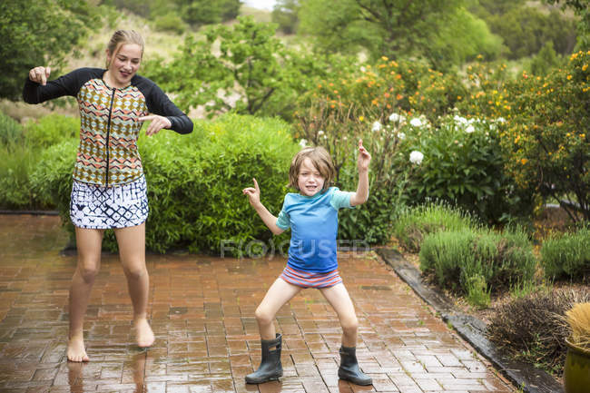 Élémentaire âge garçon avec adolescent soeur danse dans la pluie . — Photo de stock