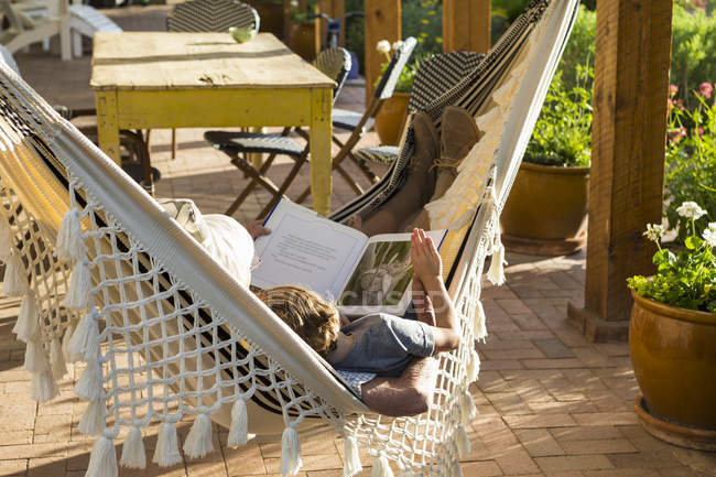 Due persone sdraiate in amaca sul portico e libro di lettura . — Foto stock