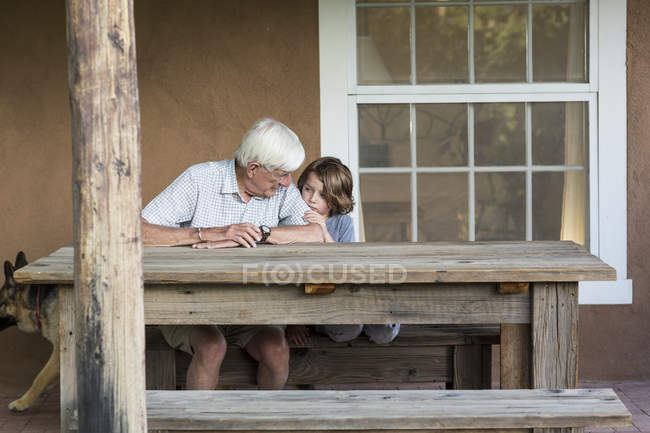 Abuelo mayor hablando con su nieto pequeño en el patio de la casa de campo . - foto de stock
