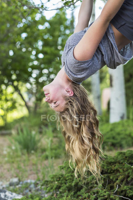 Blonde teenage girl hanging upside down from tree. — Stock Photo