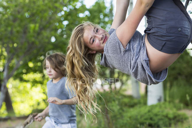 Blonde teenage girl hanging upside down from tree in garden. — Stock Photo