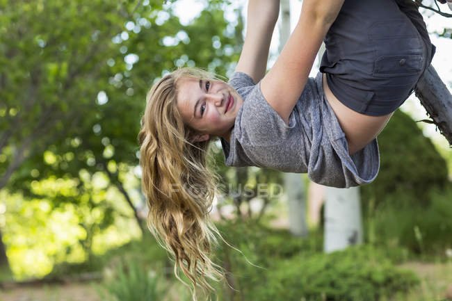Блондинка дівчина-підліток висить догори ногами з дерева в саду . — стокове фото