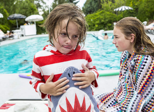 Ragazzino con sorella adolescente seduto a bordo piscina . — Foto stock