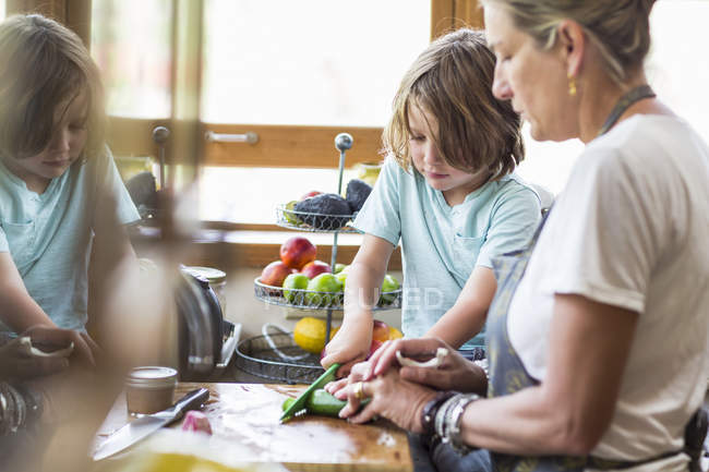 Mãe e filho pequeno cortando legumes e fazendo salada na cozinha . — Fotografia de Stock