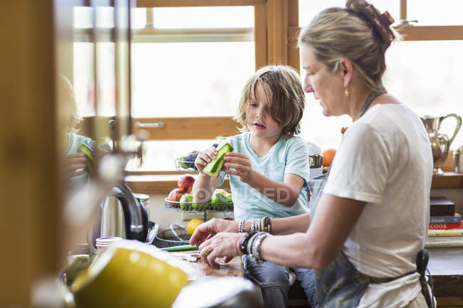 Mother and little son cutting vegetables and making salad in kitchen. — Stock Photo