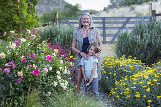 Senior grandmother and little grandson posing by roses in garden. — Stock Photo