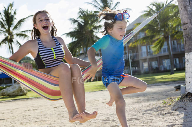 Blonde teenage girl in hammock with little brother. — Stock Photo