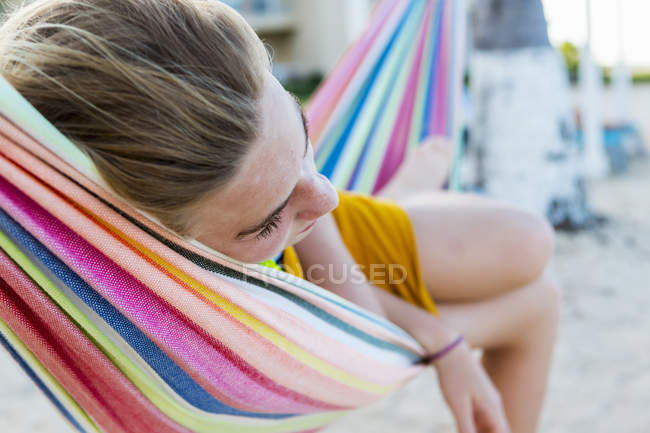 Chica adolescente rubia descansando en hamaca colorida en la playa . - foto de stock