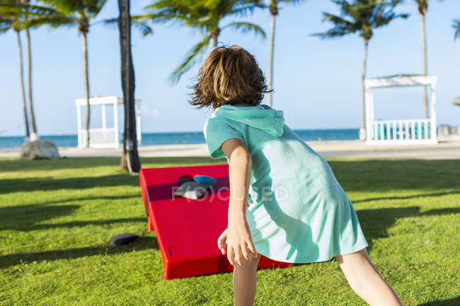 Vista posteriore del ragazzo lanciando beanbag sulla costa tropicale
. — Foto stock