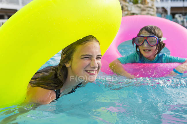 Hermanos jugando en la piscina con carrozas de colores . - foto de stock