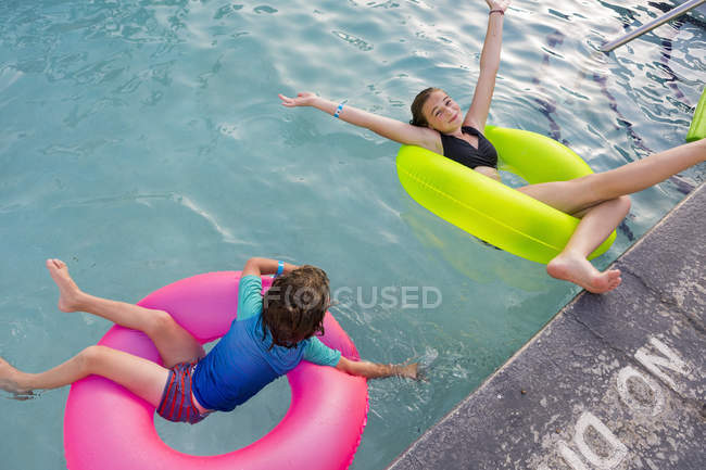 Irmãos brincando na piscina em flutuador colorido . — Fotografia de Stock